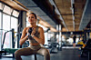 Kvinde i sportstøj laver squat med kettlebell i et lyst fitnesscenter.