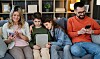 Familie på fire sidder i sofaen og bruger hver deres mobil og tablet.