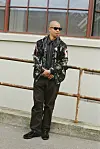 Silas Adler i mørkt streetwear står ved rækværk foran lys industribygning