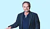 Carl-Johan i mørk jakke står foran lys blå baggrund
