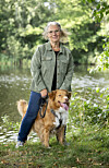 Jannie Rydahl Bjerre står ved en sø med sin hund i grønt parkområde.