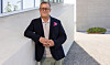 Oliver Müller i blazer læner sig op ad hvid mur foran moderne bygning